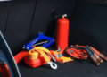 collection of emergency items in trunk of car: red triangle, red fire extinguisher, jumper cables, gloves, and more.