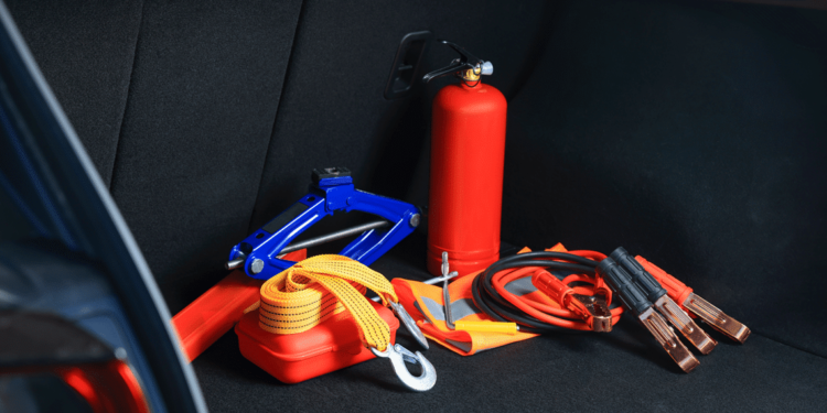 collection of emergency items in trunk of car: red triangle, red fire extinguisher, jumper cables, gloves, and more.